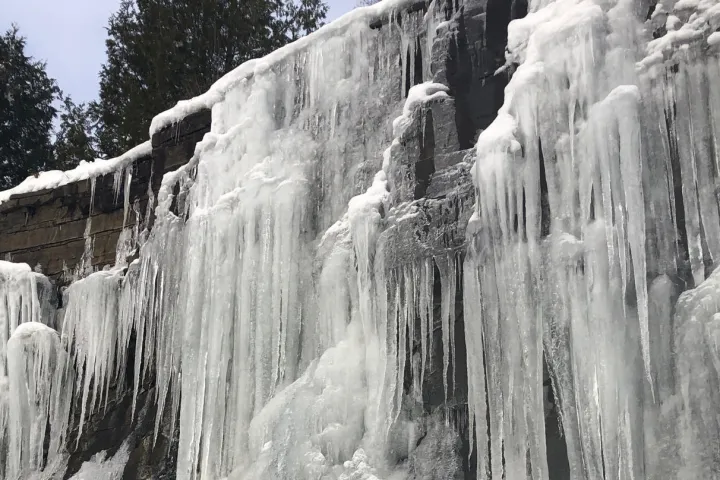 a waterfall with trees on the side of a snow covered mountain