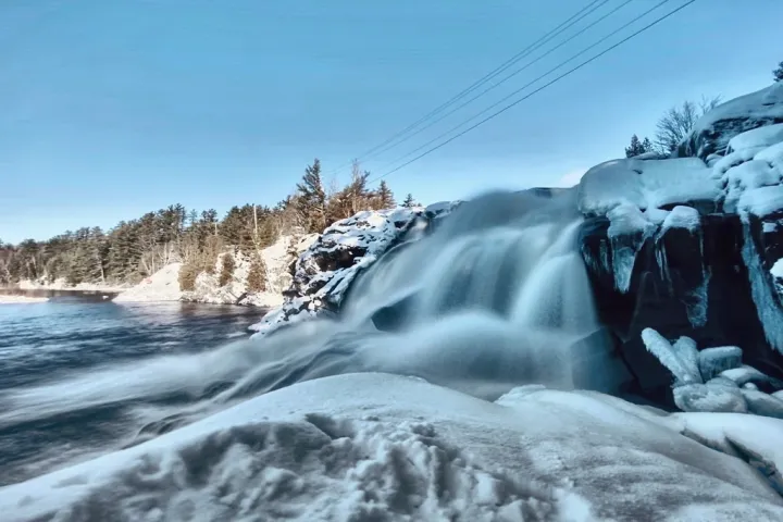 a waterfall with trees on the side of a snow covered slope