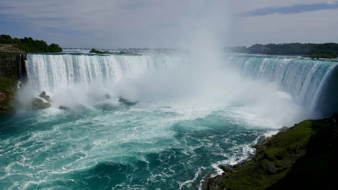 Panoramic view of a large waterfall with mist and green water.