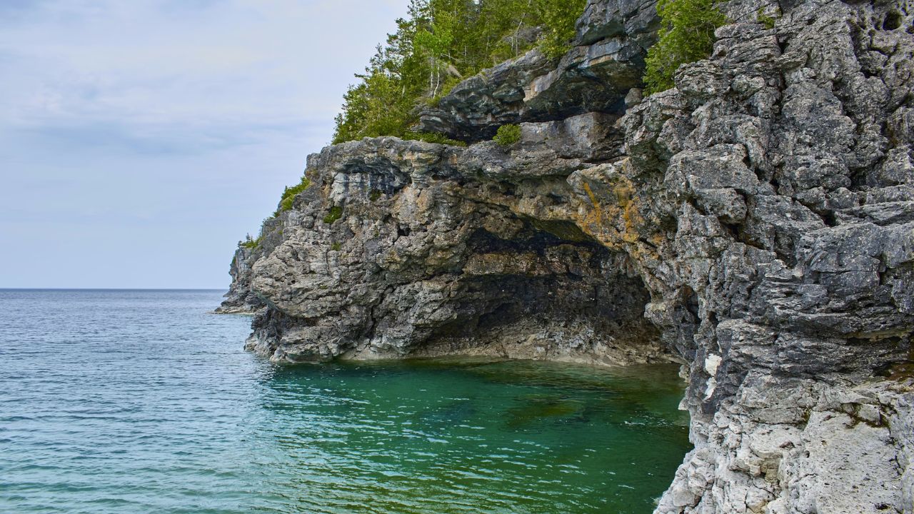Rocky cliff over turquoise water with cloudy sky background.