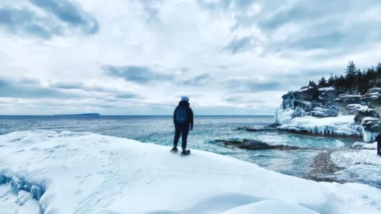 Person standing on snowy cliff overlooking a frozen icy coastline.