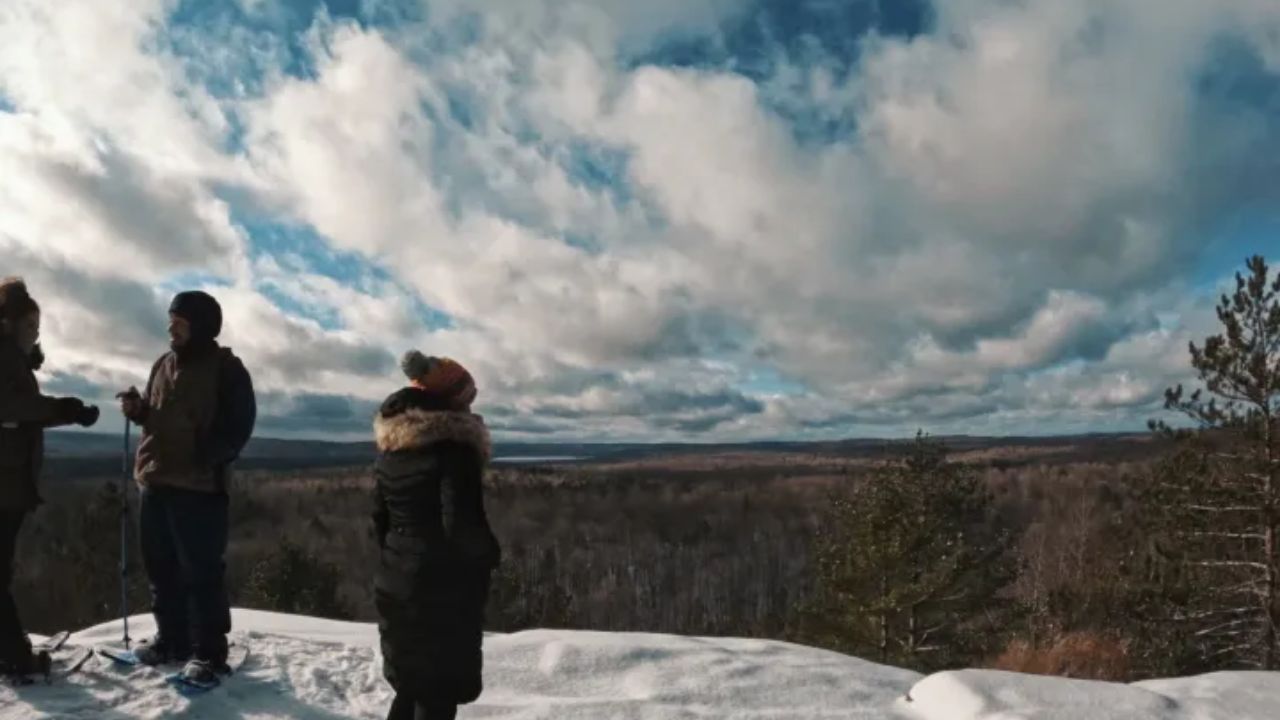Three people standing on a snowy cliff overlook at Algonquin Provincial Park