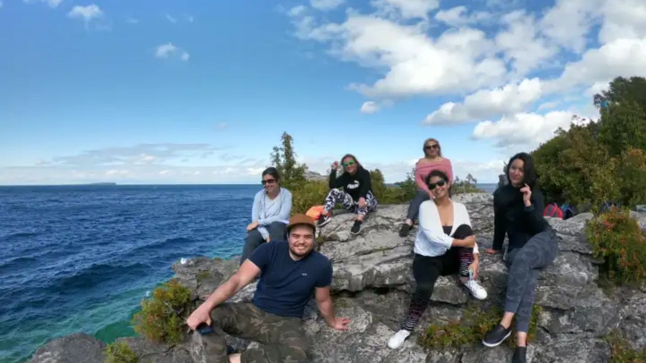 People sitting on rocky cliffs of the Bruce Trail overlooking a blue lake on a sunny day