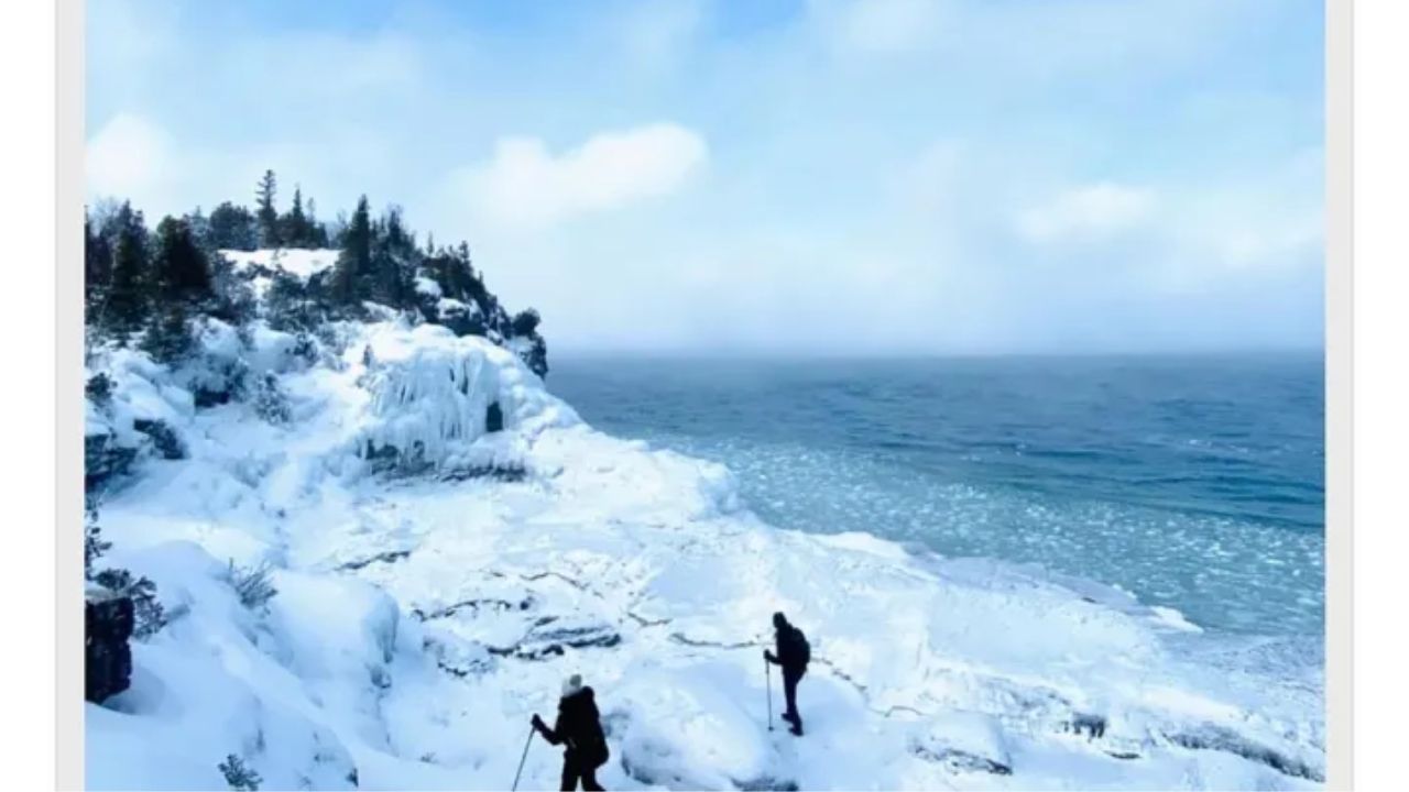 Two people hiking the Bruce Trail along a snow-covered rocky shoreline beside a frozen cliff