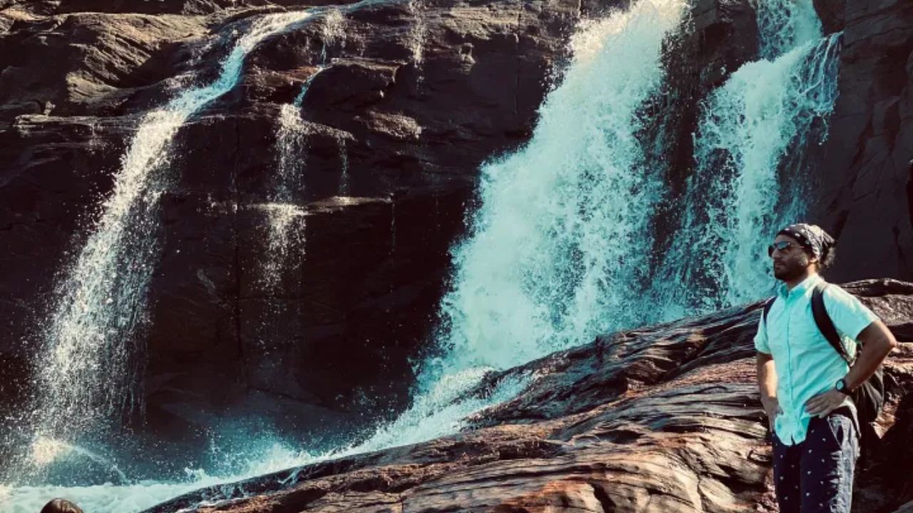 A man standing on rocky terrain beside a powerful waterfall cascading down in Muskoka