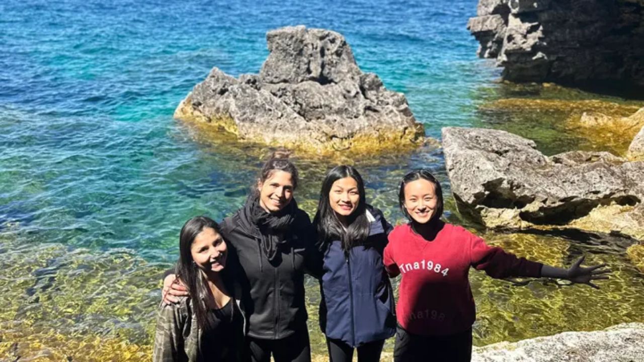 Women standing on rocky shore beside clear blue water and cliffs at Bruce Peninsula