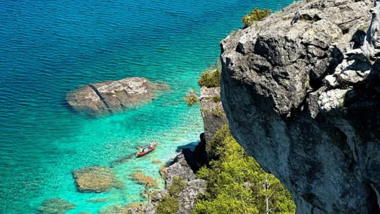 Kayaker paddling in turquoise water below a rocky cliff viewpoint at Lion’s Head Lookout