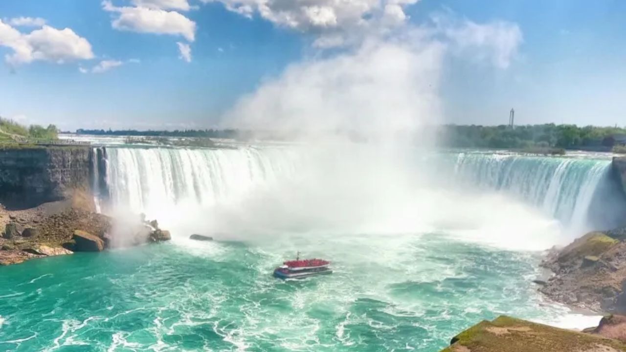 Boat near the base of Niagara Falls with mist rising above turquoise water