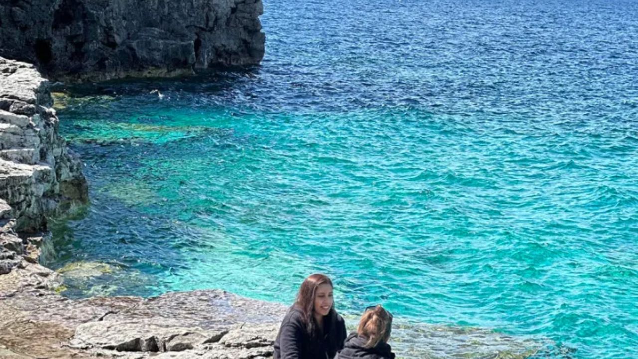 People sitting on rocky shore beside turquoise water and cliffs at Bruce Peninsula