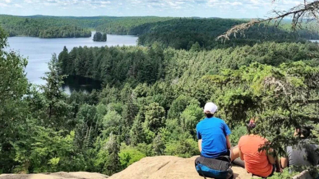 Two hikers sitting on a rocky overlook above a forested lake and islands.