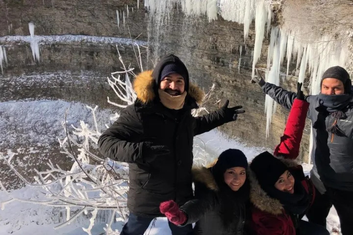 Group of travellers posing beside frozen waterfalls and large icicles during a winter Niagara adventure