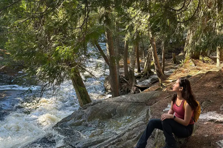 Hiker sitting near flowing water surrounded by trees
