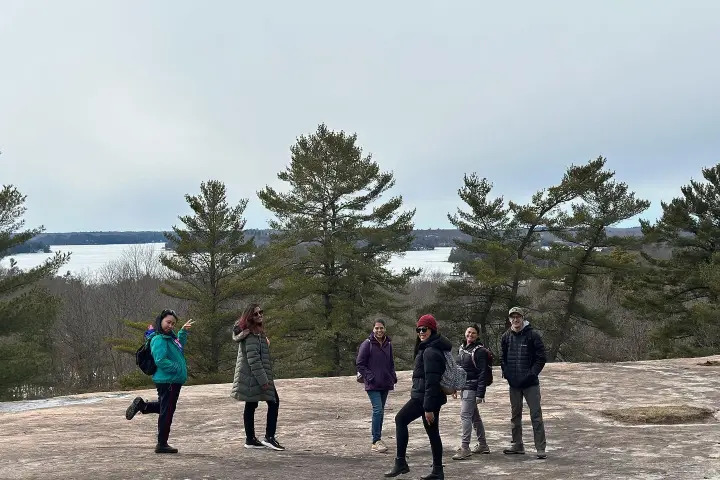 Hiking group enjoying a scenic rocky viewpoint overlooking lakes and pine forests in Muskoka