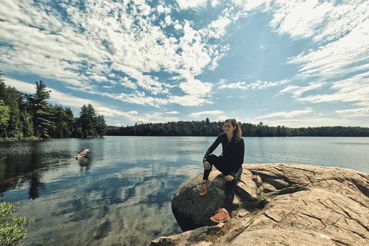 Woman relaxing on rock beside calm lake in Algonquin Park wilderness