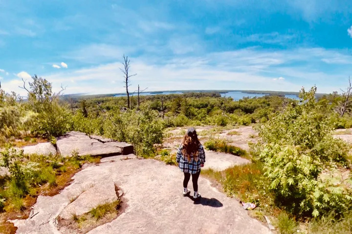 Woman standing on rocky trail overlooking forest and lake