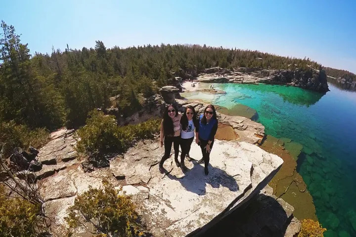 Women posing on rocky cliff overlooking clear water in Bruce Peninsula