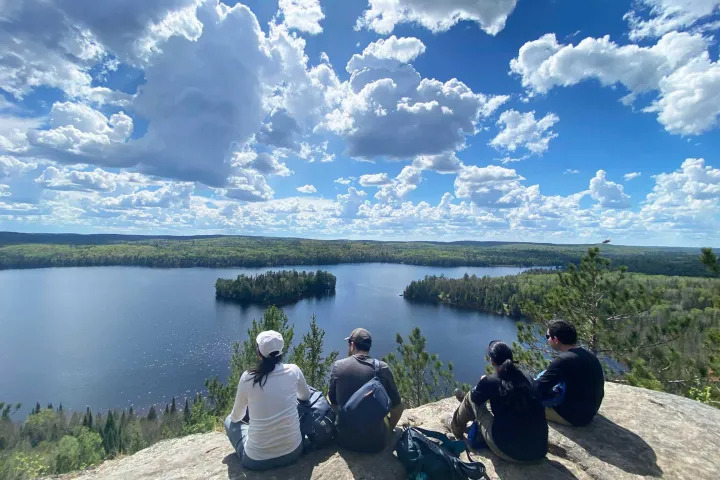 Hikers enjoying a panoramic cliffside view overlooking a pristine Algonquin Park lake and forest landscape.