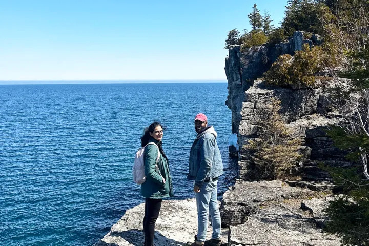 Hikers standing on dramatic limestone cliffs overlooking the crystal-blue waters