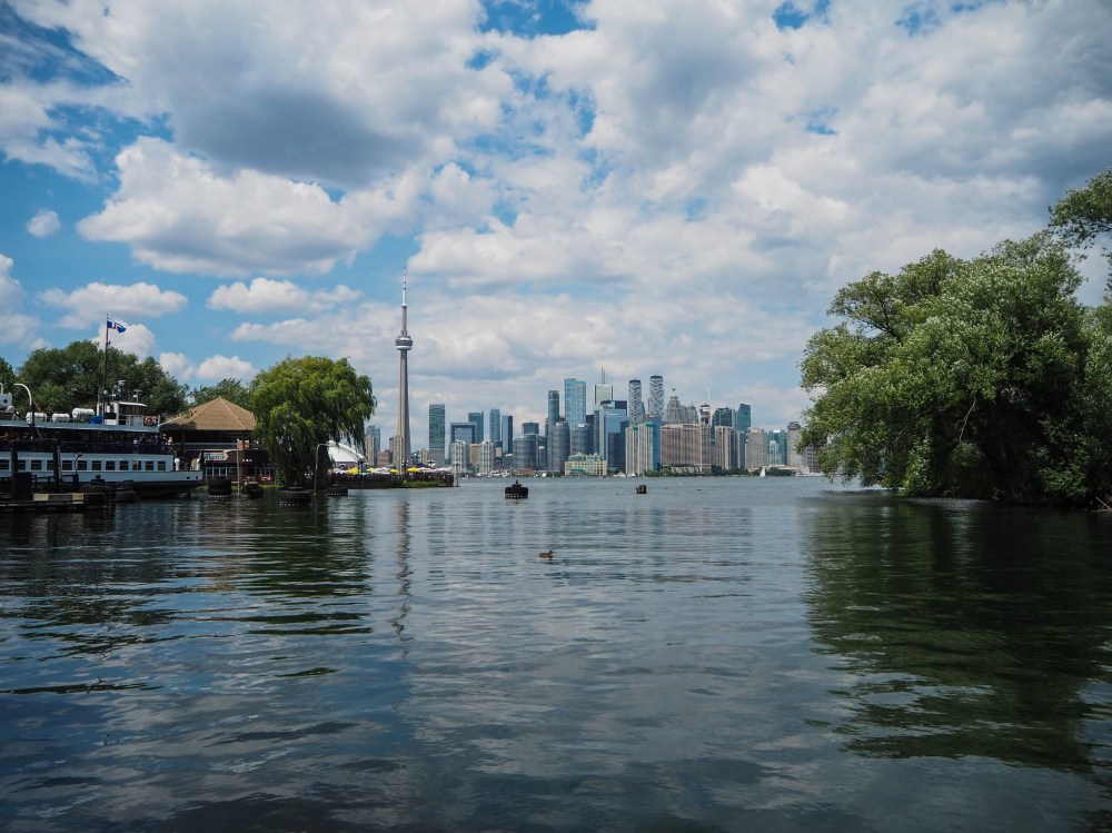 Toronto skyline viewed across Lake Ontario with the CN Tower reflected in calm waterfront waters
