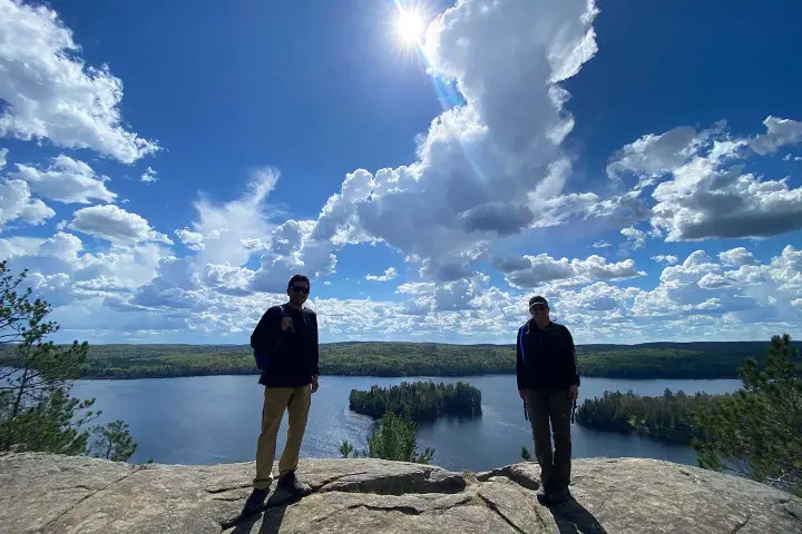 Visitors standing atop a cliffside viewpoint overlooking a pristine lake and forested landscape in Algonquin Park.