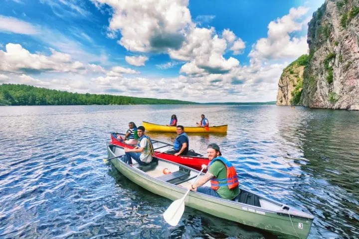People canoeing on a lake near cliffs under a blue sky with clouds.