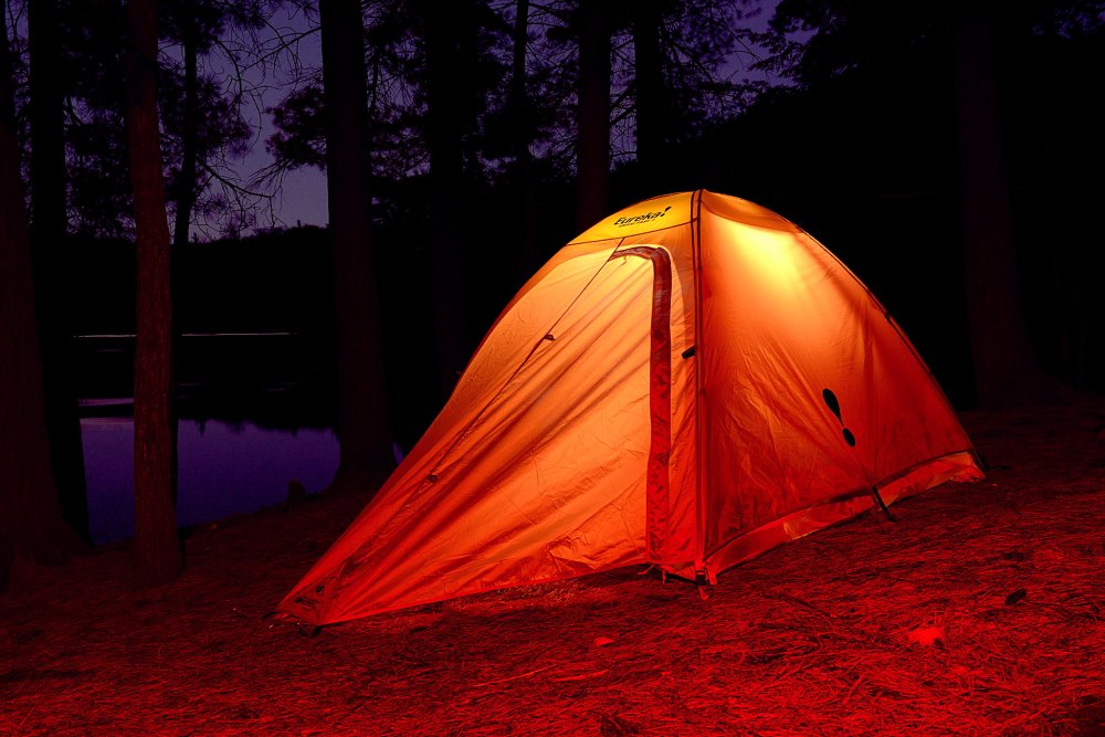 Glowing orange and yellow Eureka camping tent pitched in Killarney Provincial Park at night near water.