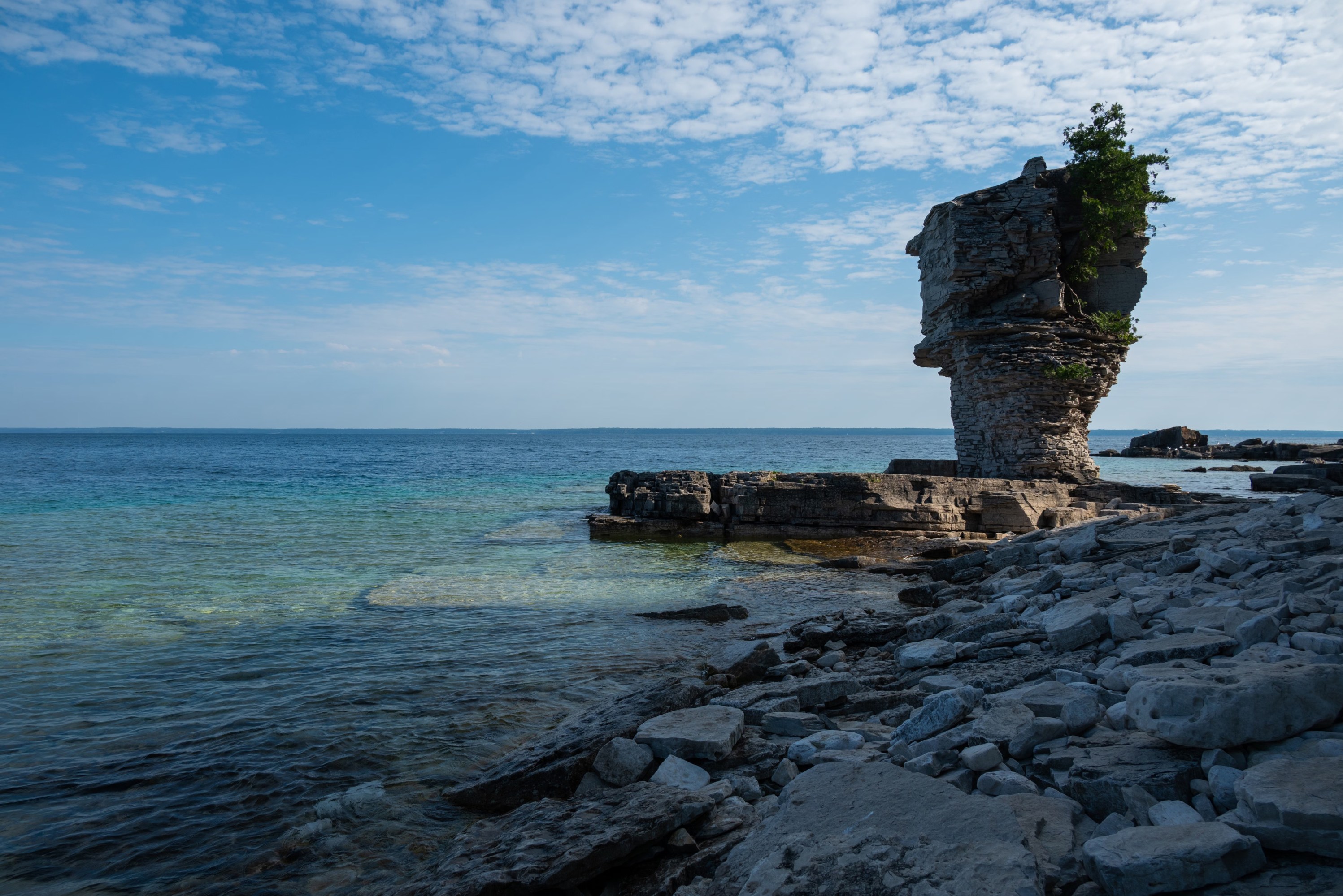 Iconic flowerpot-shaped sea stack rising beside the rocky shoreline and clear blue waters near Tobermory, Ontario