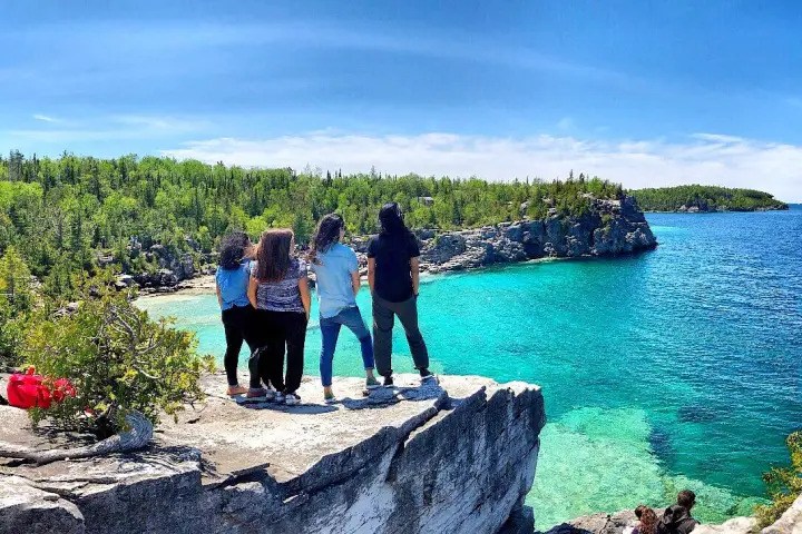 Visitors enjoying panoramic views of brilliant turquoise water, limestone cliffs, and forested shoreline near Tobermory, Ontario.