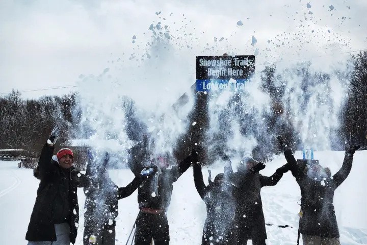 Friends celebrating by throwing fresh snow into the air on a winter trail.