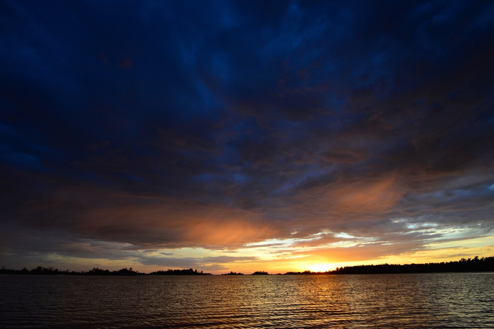 Golden sunset over a tranquil lake beneath a cloudy evening sky.