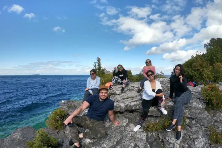 Group of friends relaxing and posing on rocky cliffs overlooking deep blue open water on a sunny day at Bruce Peninsula.