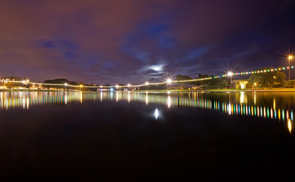 Night reflection of decorative string lights along a waterfront promenade of Canoe Lake