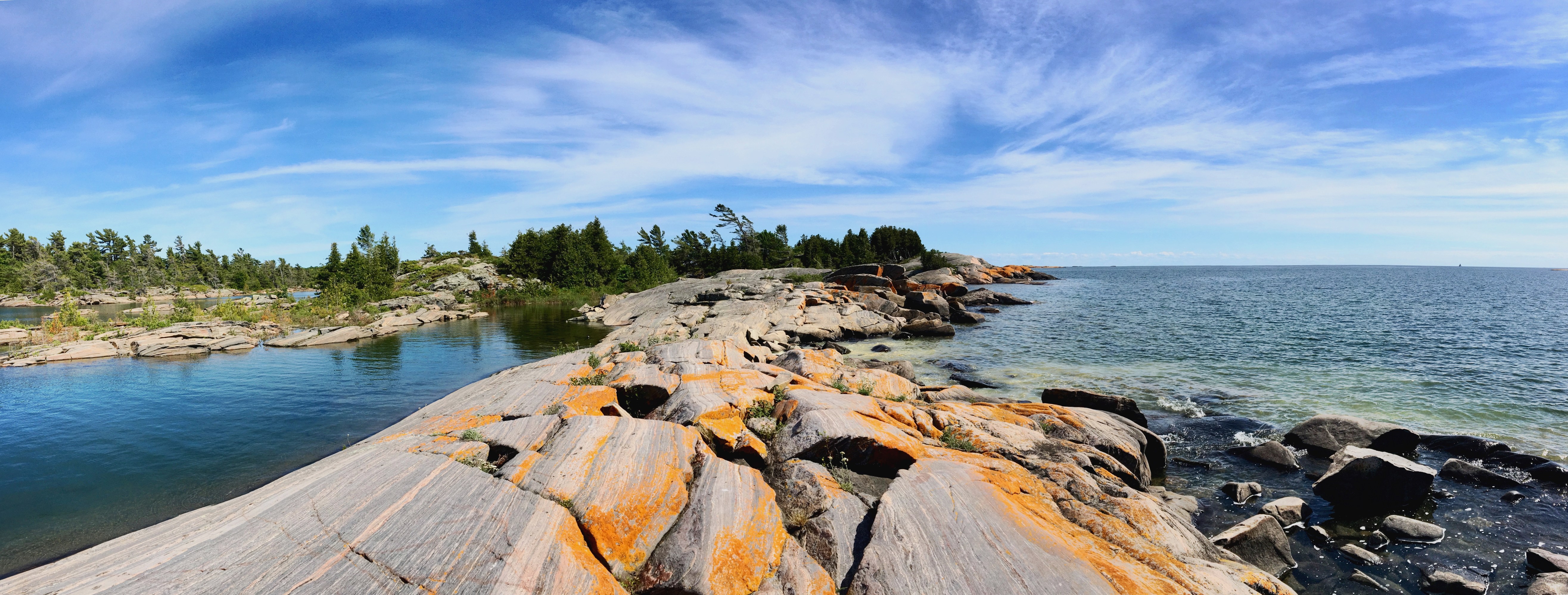 Panoramic view of orange lichen-covered rocks along a calm lake shoreline.